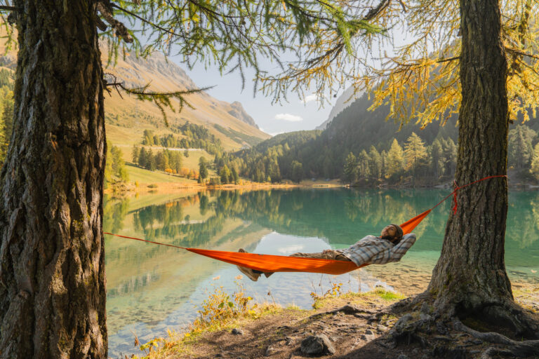 Man resting in hammock at beautiful lake in Swiss Alps in autumn