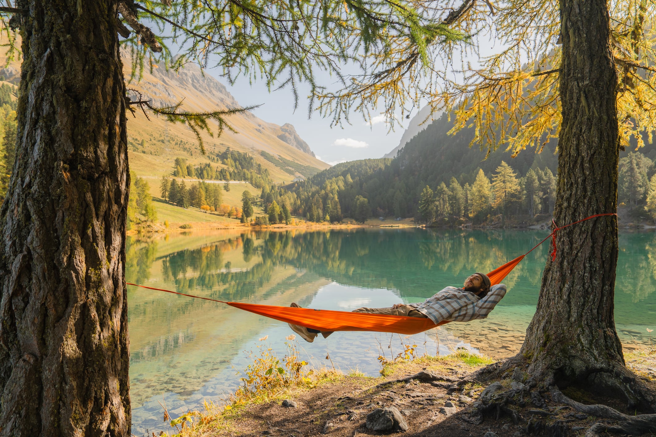 Man resting in hammock at beautiful lake in Swiss Alps in autumn